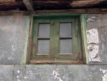 A window with four panes of glass is dirty and has a green frame. The window is located on a building with a lot of peeling paintの写真素材