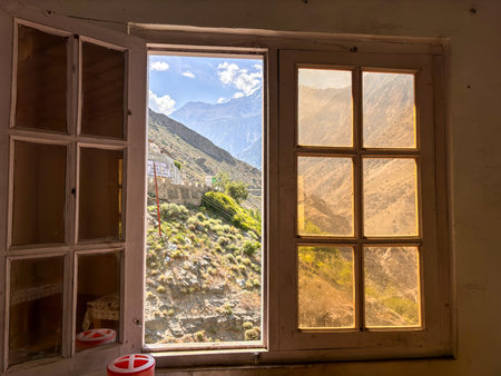 A window with a view of mountains and a house. The window is open and the view is very beautiful