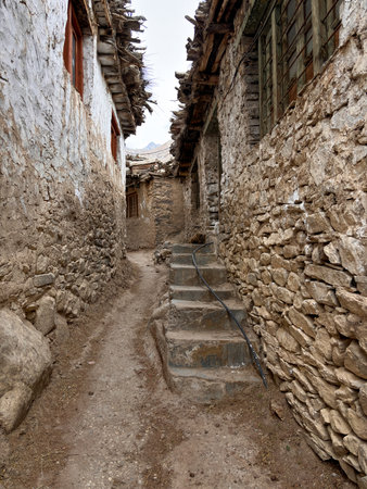 A narrow alleyway with a stone wall on either side. The alleyway is lined with stone and has a dirt floor. There is a staircase leading up to the top of the alleywayの写真素材