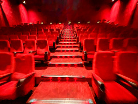 A red movie theater with rows of red chairs. The chairs are empty and the theater is darkの写真素材