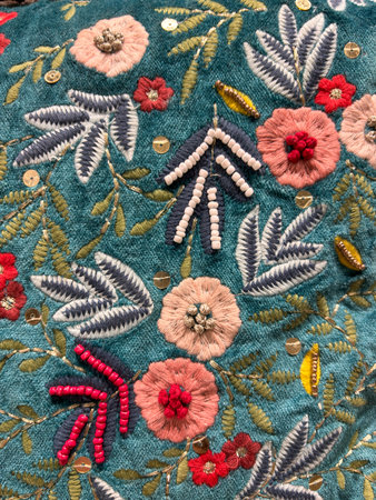 A blue and green floral patterned fabric with red flowers embroidered on it. The flowers are made of beads and the fabric is embroidered with a lot of detailの写真素材