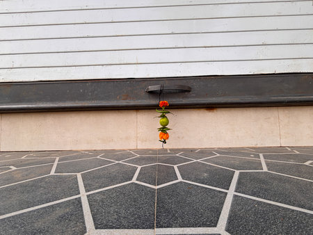A hanging garland of flowers and vegetables, including peppers, is suspended from a metal door...