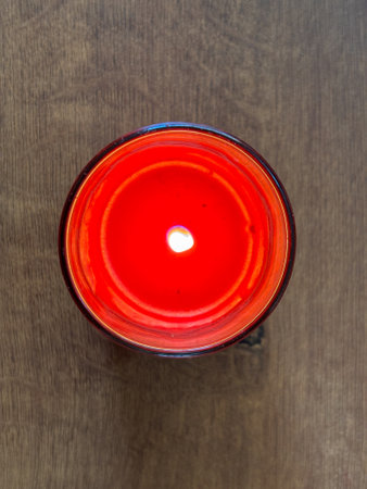 A red candle is lit in a glass jar. The flame is visibleの写真素材