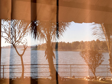 A curtain is open to reveal a beautiful view of the ocean and a beach. The scene is peaceful and relaxing, with the water and trees providing a serene atmosphereの写真素材