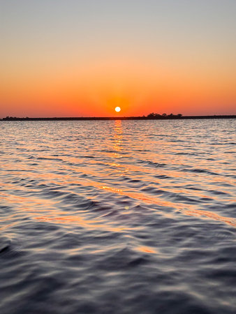 The sun is setting over the water, creating a beautiful orange and pink sky. The water is calm and...