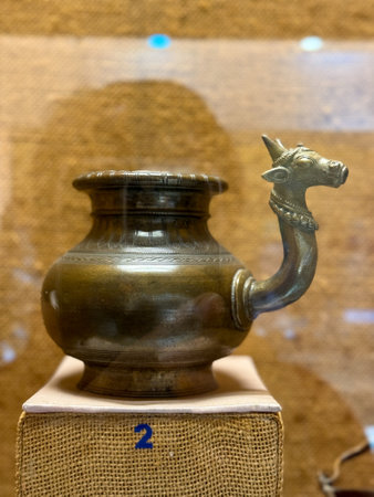 A bronze pot with a horned head sits on a wooden block.の写真素材