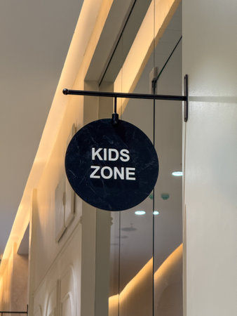 A sign hanging on a door that says "Kids Zone". The sign is black and white and is hanging from a metal barの写真素材