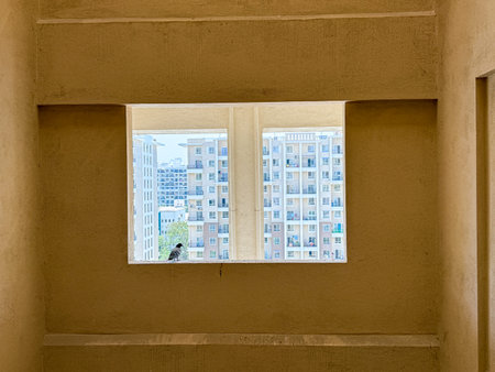 A bird is sitting on a ledge in front of a building. The bird is looking out the window, and the...