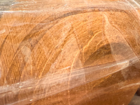 A piece of bread is wrapped in plastic. The bread is brown and has a slightly rough textureの写真素材