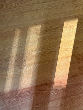 A wooden floor with a sunbeam shining through a window, casting shadows on the floor. The shadows are long and thin, creating a sense of depth and dimension in the sceneの写真素材