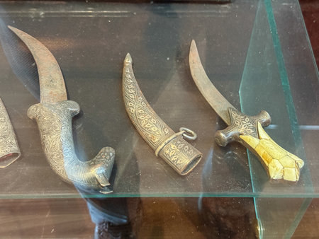 Three swords are displayed on a glass shelf. The swords are old and have intricate designs on them. The display is in a museum or a storeの写真素材