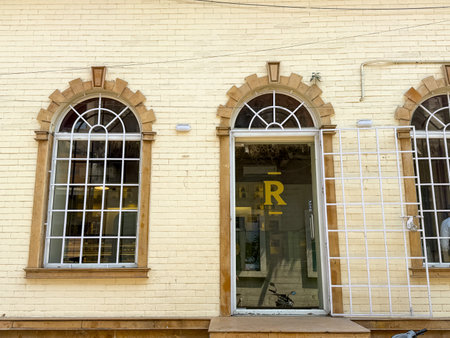 The building has a white facade with a yellow lettering that says R. The windows are arched and the...