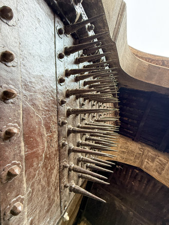 A close up of a door with many spikes on it. The spikes are arranged in a row and are pointing upwards. The door is old and has a rustic appearance. Concept of danger and cautionの写真素材