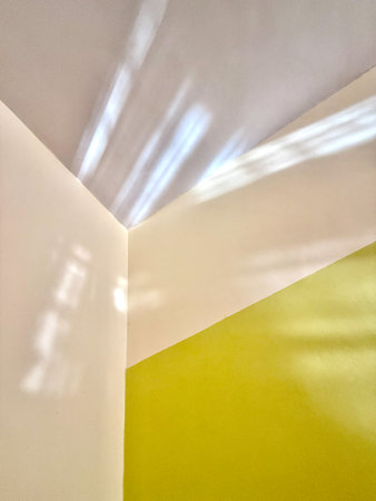 A corner of a room with a yellow wall and a white wall. The white wall has a shadow on itの写真素材