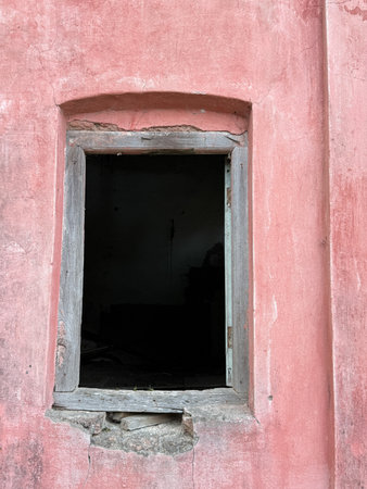 A window is open in a room with a pink wall. The room is empty and the window is the only source of lightの写真素材