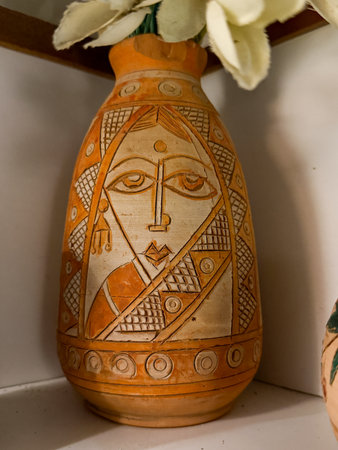 A vase with a woman's face on it sits on a shelf. The vase is orange and white, and the woman's face is drawn in brown.の写真素材