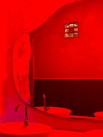 A bathroom with a red wall and a mirror with a light on it. The light is on the right side of the mirrorの写真素材