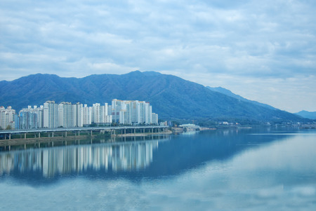 Big mountain and high building with blue sky reflection mirror on water riverの写真素材