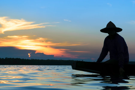 asian fisherman silhouette fishing on the both during sunset.