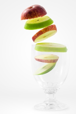 Slices of red and green apple falling into a glass の写真素材