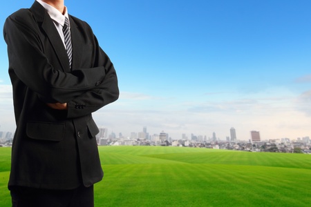 Businessman standing near grass field blue sky with skyscraper background の写真素材