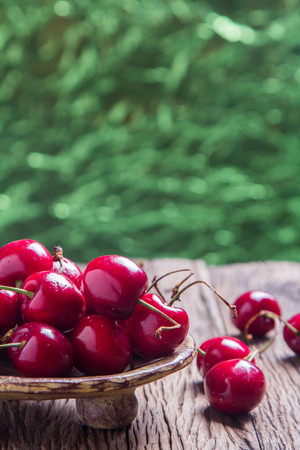Cherries on wooden table with abstract circular green bokeh background, Close up for design workの写真素材
