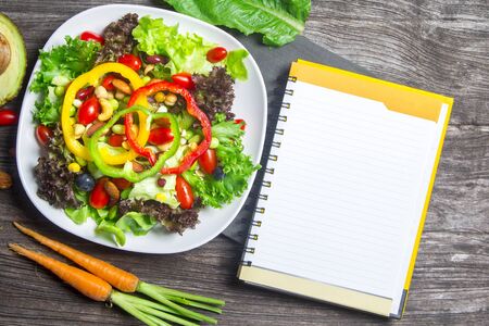 fresh vegetable salad with notebook paper on wood table background, top viewの写真素材