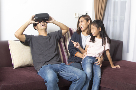 Happy asian family at home wearing virtual reality goggles in modern coworking studio. Smartphone using with VR headset.の写真素材