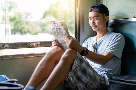 Asian man traveling backpacker reading map sit on the old train seat at Thailandの写真素材