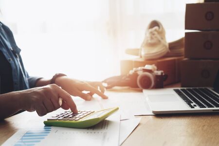 Women hand doing finances and calculate on desk about cost at home office, Online selling e-commerce shipping idea concept freelance start up small business ownerの写真素材