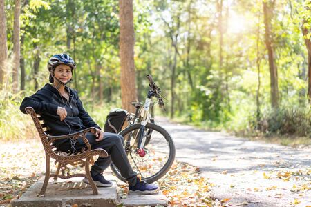 Senior asian woman bicycle with sitting in the park, With using smart phone and listening to musicの写真素材