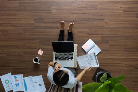 Top view woman working on laptop with talking smart phone on wooden floor, Work at home idea conceptの写真素材