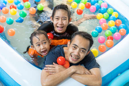 Asian happy family father and daughter playing in the swimming pool at home, and coloured ballsの写真素材