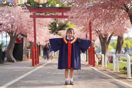 Happy Asian little girl in graduation. under the blossom sakura tree backgroundの写真素材