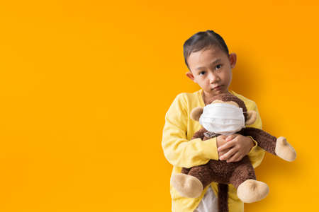 Asian child girl hugging doll wearing mask on yellow backgroundの写真素材