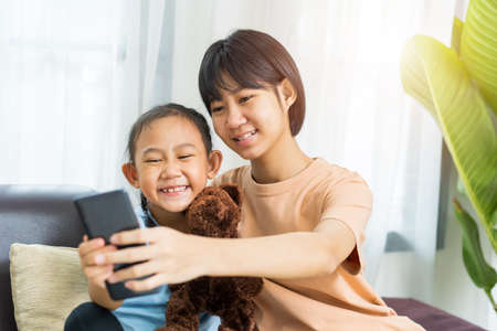 Happy Asian girl with sister play on the smart phone together at homeの写真素材