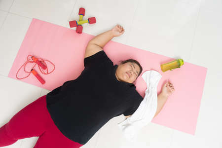 Asian woman fat exhausted with excess weight lying on floor after training at home, Exercising weight loss and recreation idea concept.の写真素材