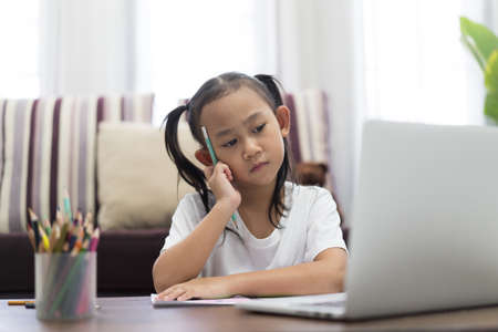 Asian girl thoughtful studying homework online lesson at home, Social distance online education idea conceptの写真素材