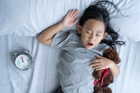 Top view child little asian girl sleeps in the bed with a toy teddy bearの写真素材