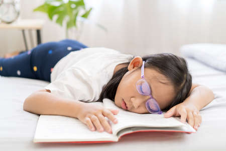 Asian child little girl sleep, tired from reading a book on the bedの写真素材