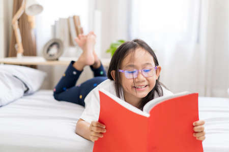 Asian child little girl reading books lying on the bed at home.の写真素材