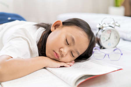 Asian child little girl sleep, tired from reading a book on the bedの写真素材