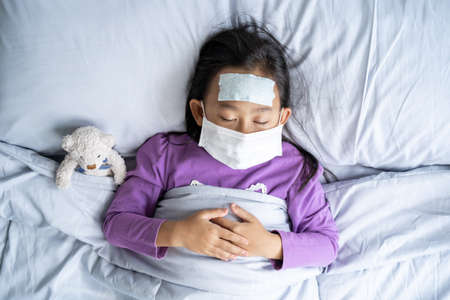 Top view Asian child girl sick with Face mask and cold cough because weak, Sick child with fever and illness in bed.の写真素材