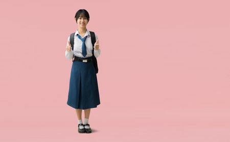 Full body Asian student girl wearing uniform with smiling giving thumbs up, isolated on pink background with Clipping paths for design work empty free spaceの写真素材
