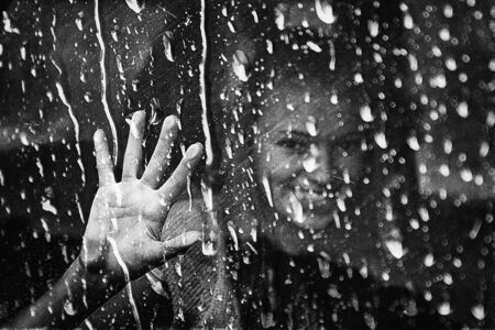 a pretty girl behind a wet windowの写真素材