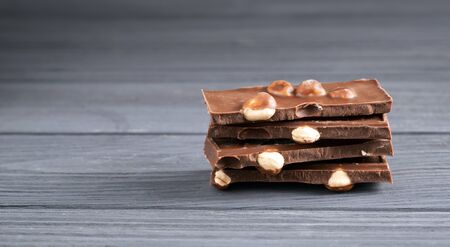 Pieces of milk chocolate with nuts on a gray wooden table. Chocolate bars with hazelnut. Sweet brown chocolate.の写真素材