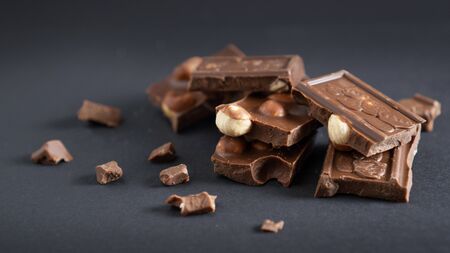 Milk chocolate bars with big nuts inside and crumbs scattered around. Beautiful bokeh on dark background. Brown chocolateの写真素材