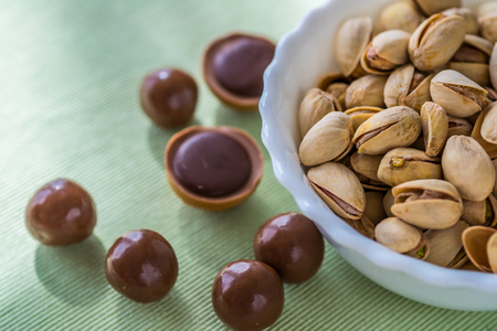 Roasted pistachios on a white bowl, chocolate bombons and caramel candies.の写真素材