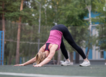 Fit caucasian girl doing yoga on the sports ground outdoor, selective focus. Dog face down pose