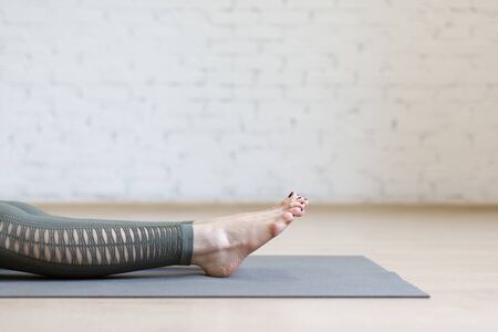 Female bare feet on the floor, close up. Caucasian woman in sporty leggings lying on the mat in loft fitness studio, selective focus. Yoga nidra, pilates, relax, body parts, exercise therapy, meditation and wellness concept.の写真素材